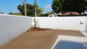 A paved outdoor area with a white wall and a small garden bed with plants. - Maison Charme 70m2 Saint Georges Oléron (Saint-Georges-d'Oléron)
