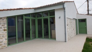 A modern building with large glass doors, a stone facade, and a green door. - Maison Charme 70m2 Saint Georges Oléron (Saint-Georges-d'Oléron)