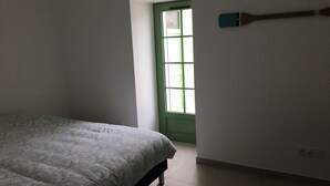 A bedroom with a bed, a green door, and a wall-mounted object. - Maison Charme 70m2 Saint Georges Oléron (Saint-Georges-d'Oléron)