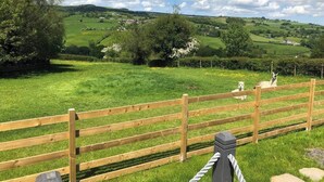 A wooden fence with a rope barrier, a grassy field, and a hilly landscape in the background. - The Shepherds Hut at Hafoty Boeth (Corwen)