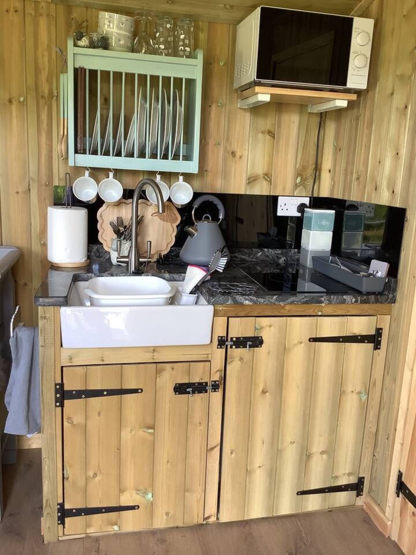 Een kleine keuken met houten kastjes, een spoelbak, een magnetron en een afdruiprek.