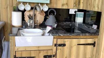 Een kleine keuken met houten kastjes, een spoelbak, een magnetron en een afdruiprek.