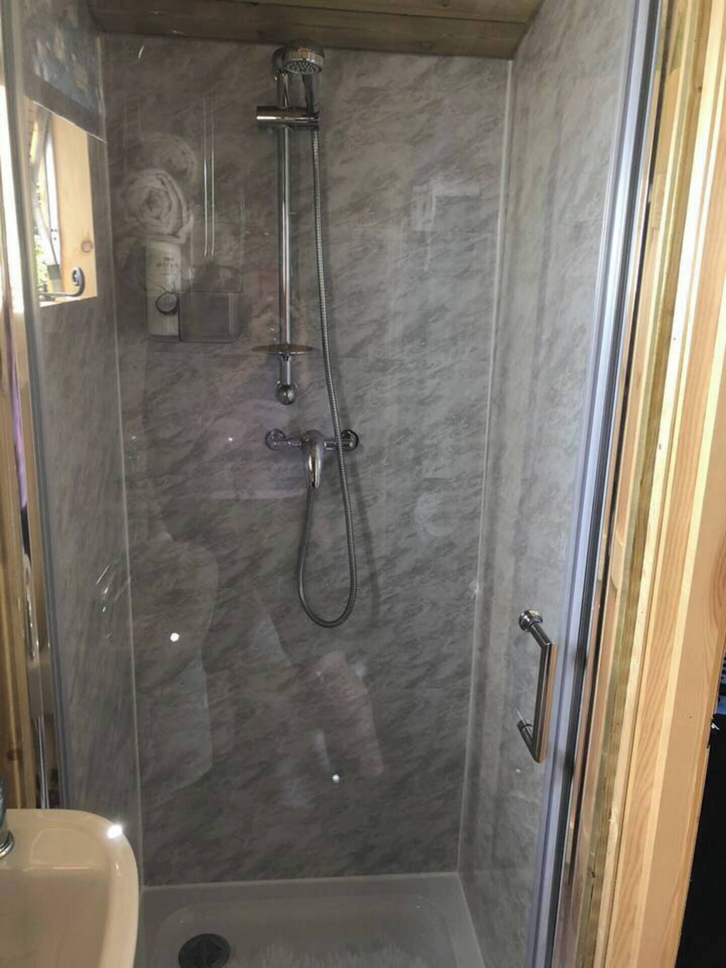 Une douche équipée d’un pommeau de douche à main et d’un pommeau de douche fixe, d’une porte en verre et d’un mur en marbre.