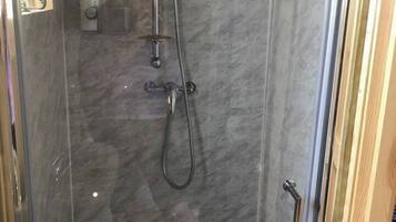 Une douche équipée d’un pommeau de douche à main et d’un pommeau de douche fixe, d’une porte en verre et d’un mur en marbre.