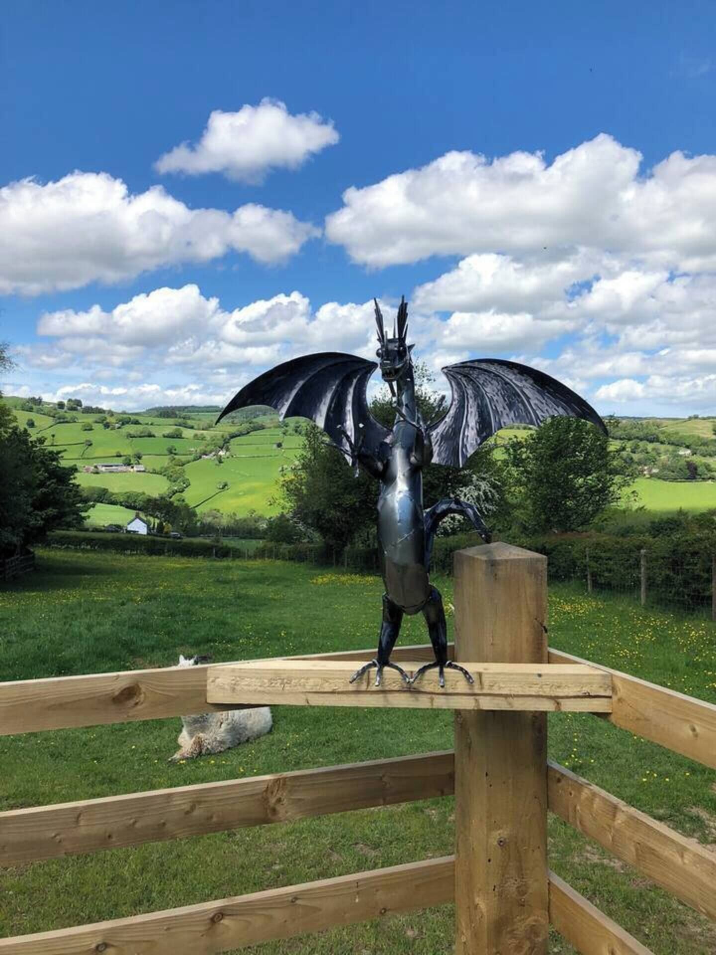 A metal sculpture of a dragon on a wooden platform in a rural landscape.