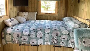 A cozy room with a curved ceiling, wooden walls, a bed with a patterned blue and white bedding, a window with a view of greenery, and a mounted TV. - The Shepherds Hut at Hafoty Boeth (Corwen)