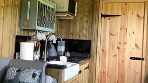 A compact kitchen with wooden walls, a sink, a stove, and a green dish rack. - The Shepherds Hut at Hafoty Boeth (Corwen)