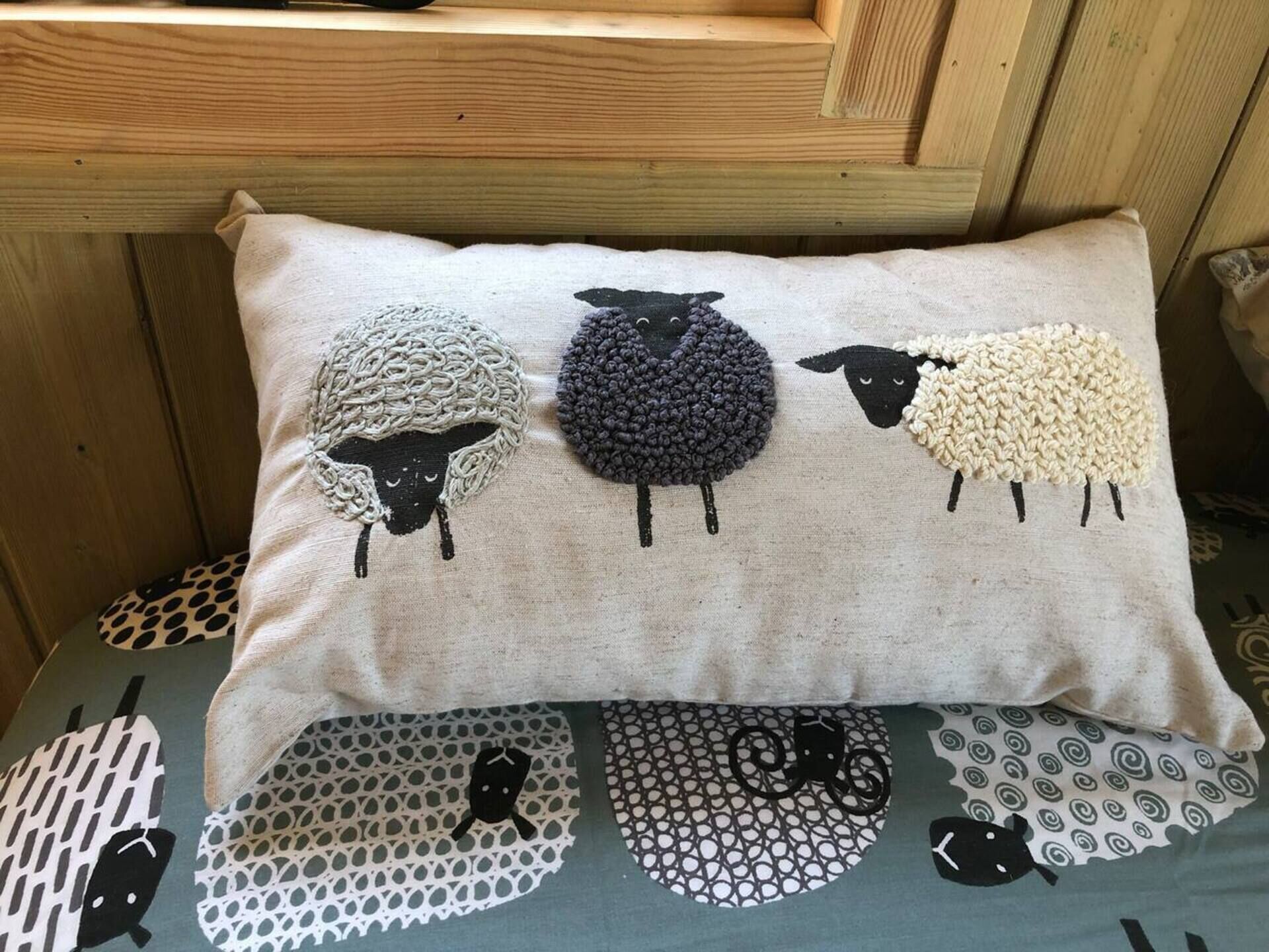 A pillow with a sheep design on a bed with a patterned bedspread.