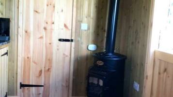 A wooden cabin interior with a black wood stove, a door, and a window.