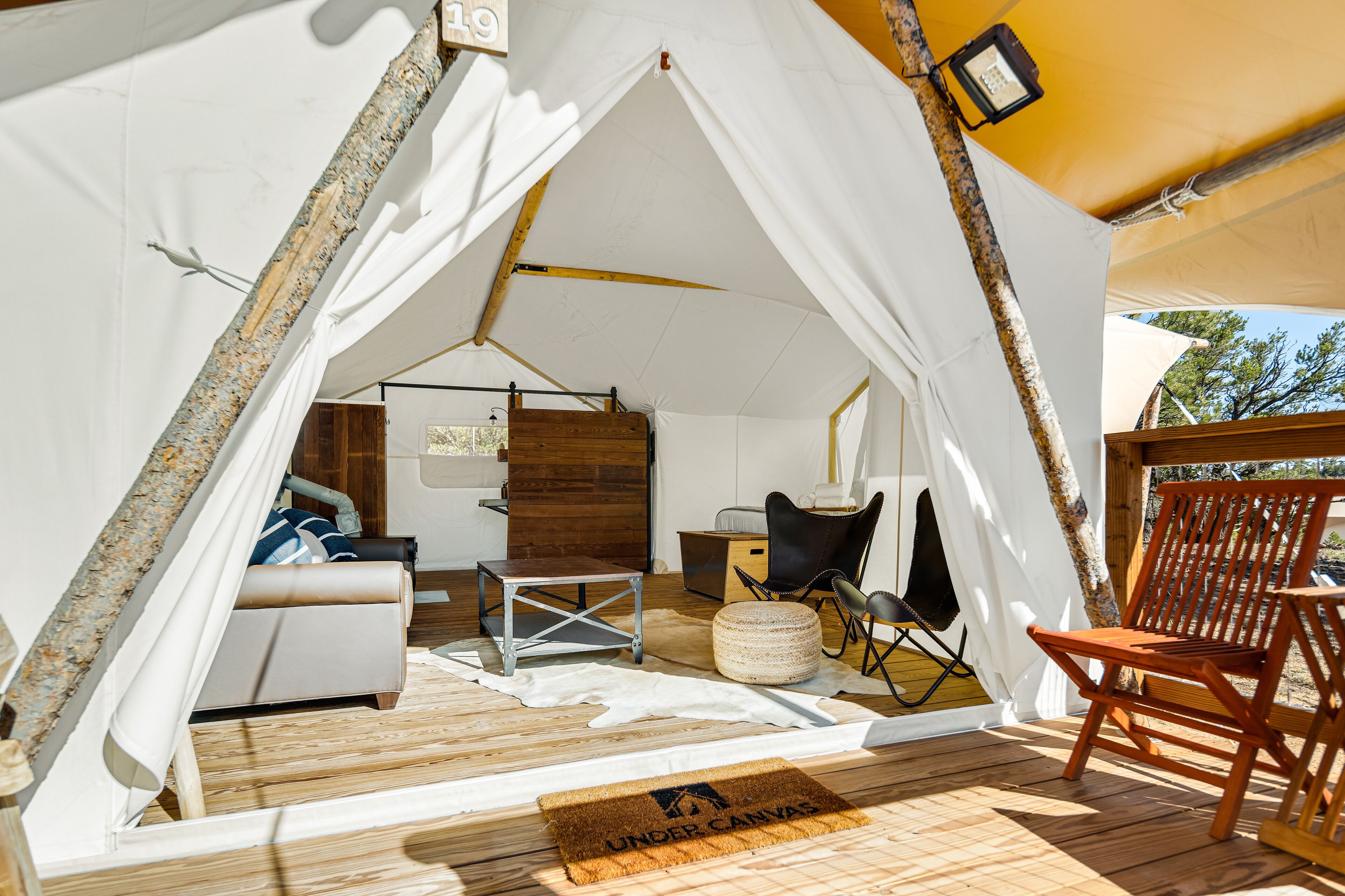 A tented accommodation with a wooden floor, a sofa, a dining area, and a chair.
