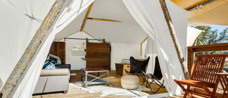 A tented accommodation with a wooden floor, a sofa, a dining area, and a chair.