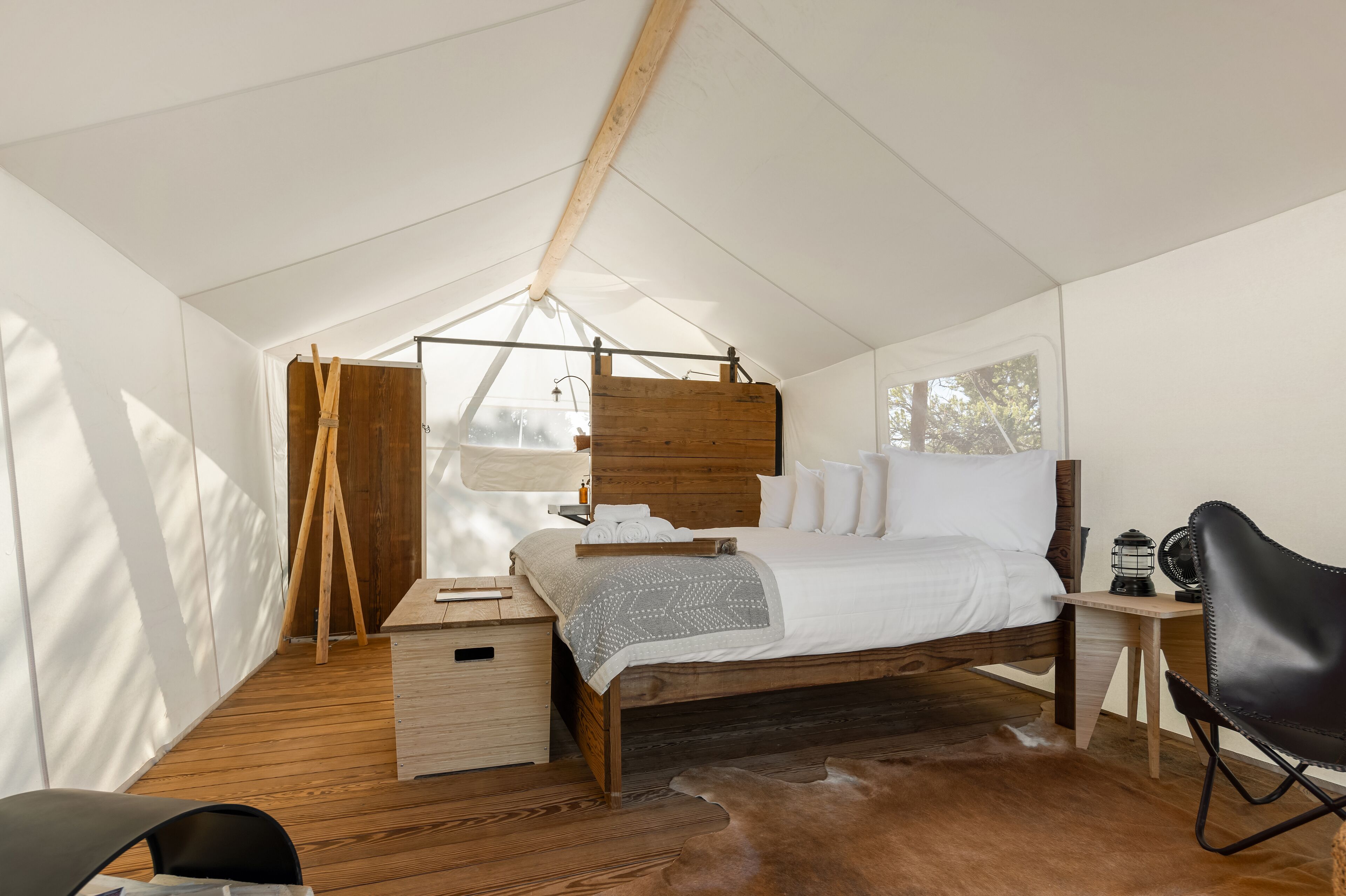 A tent-style bedroom with a wooden bed, a small desk, a chair, and a hanging wooden board.