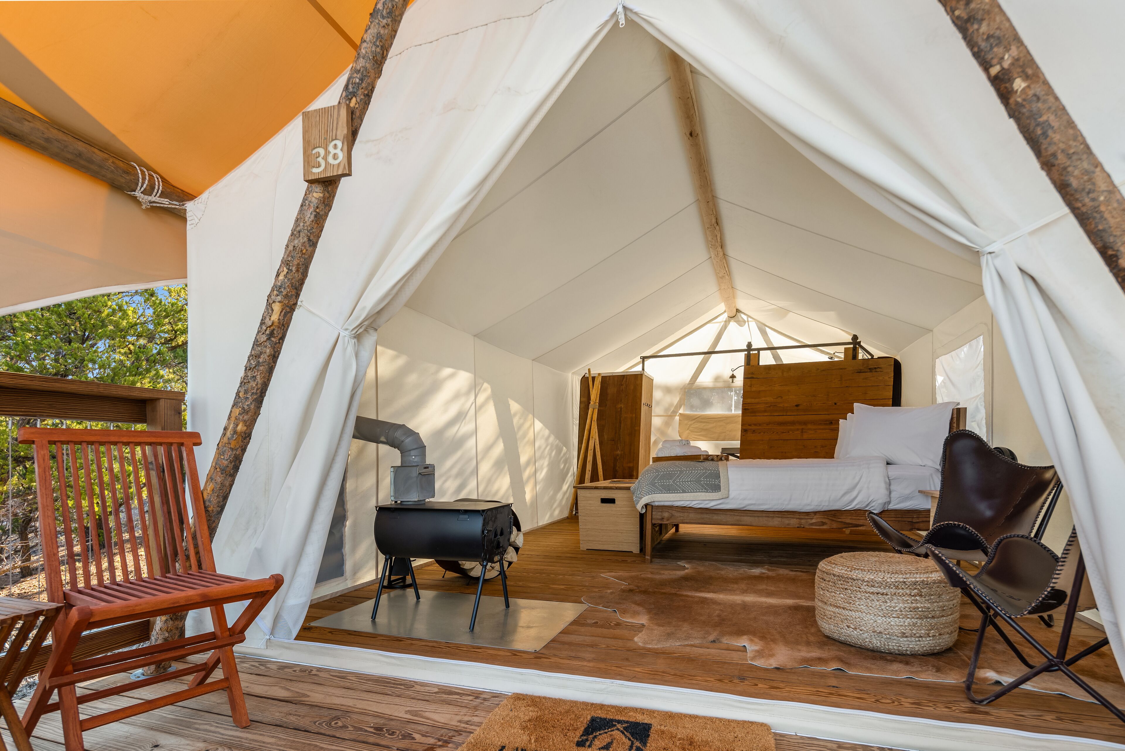 Een tentaccommodatie met een bed, een houten stoel, een klein tafeltje en een open haard.