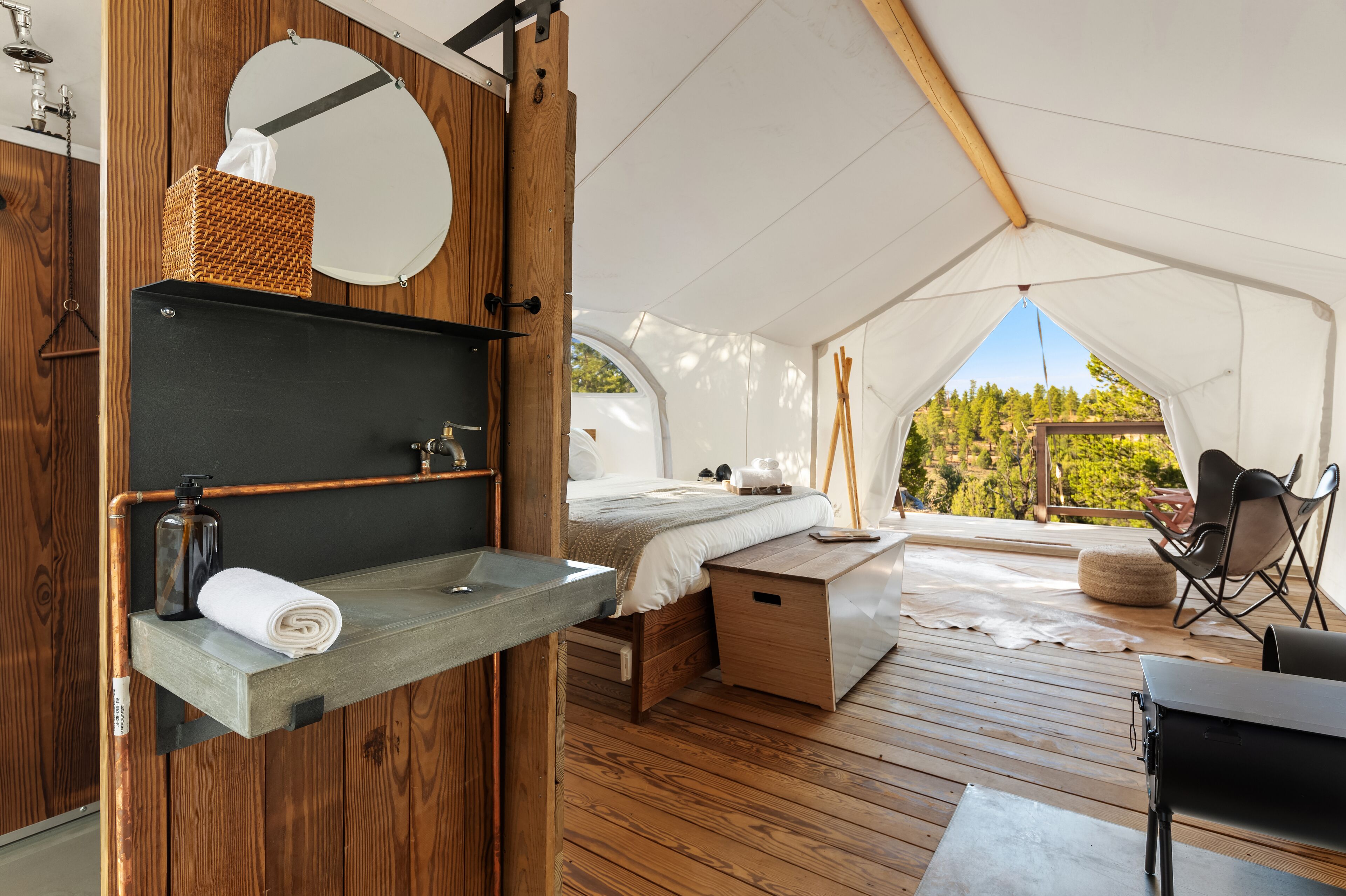 Eine Zelthütte mit Holzinnenraum, einem Bett, einem kleinen Tisch und Blick ins Freie.