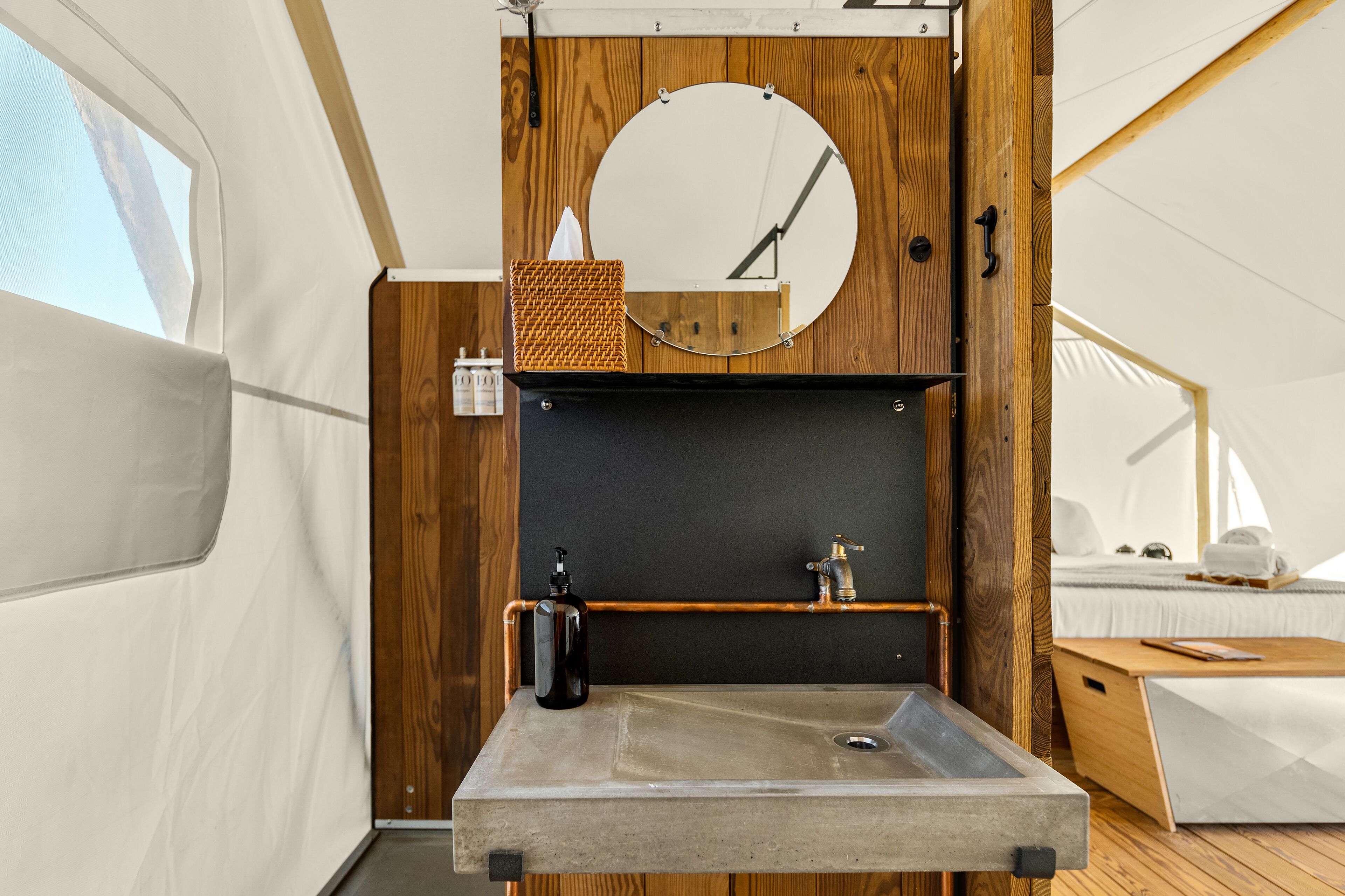 A compact, modern bathroom with a concrete sink, wooden accents, a round mirror, and a small shelf.