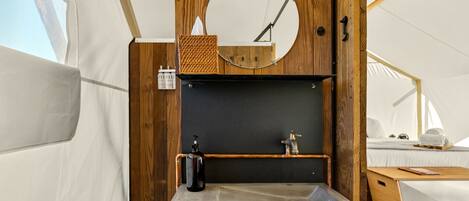 A compact, modern bathroom with a concrete sink, wooden accents, a round mirror, and a small shelf.