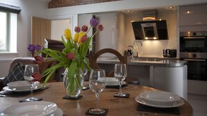 A dining area with a table set for four, a vase with tulips, and a kitchen in the background. - The Shippon -hot Tub ext chg - Superking-log Fire (Preston)