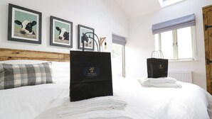 A hotel room with a neatly made bed, two black gift bags on the bed, and framed artwork on the wall. - The Shippon -hot Tub ext chg - Superking-log Fire (Preston)
