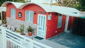 A red building with a white door and window shutters, a small porch, and a white fence.