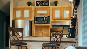 A modern kitchen with wooden cabinets, a microwave, and a bar area with two stools.