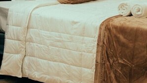 A neatly made bed with white bedding and a brown throw pillow, a rolled-up towel, and a dark headboard.