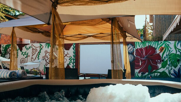 A hot tub area with a view of a room featuring a large window, a clock, and a wall with floral and leaf patterns.