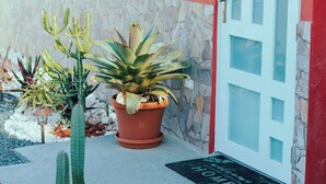 A red building with a white door and windows, a sign reading "This is our happy place," and potted plants in front.