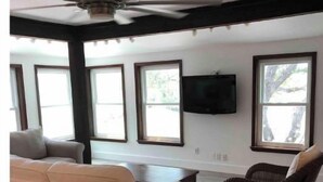 A spacious living room with a ceiling fan, large windows, a flat-screen TV, a white sofa, a wicker chair, and a wooden coffee table. - Hop/Skip/Jump to Canyon Lake - 3 BR, 2 Bath (Canyon Lake)