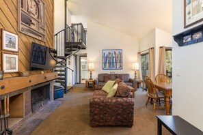 A cozy living room with a fireplace, a staircase, and a dining area with wooden furniture. - Condo Nestled in the Pines/Shared Pool and Hot Tub/On Shuttle Route to Slopes (Keystone)