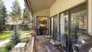 Une véranda couverte avec des sièges d’extérieur, un barbecue et une vue sur le jardin arrière.