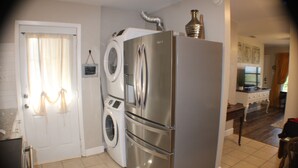 A compact kitchen with a stainless steel refrigerator, a built-in washing machine, and a dining area with a table and chairs. - The View at 5 Hills (Copperas Cove)