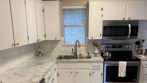 A kitchen with white cabinets, a dishwasher, a stove, a microwave, and a window with blinds. - The View at 5 Hills (Copperas Cove)
