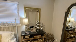 A bedroom with a bed, bedside table, dresser, mirror, and a patterned rug. - The View at 5 Hills (Copperas Cove)
