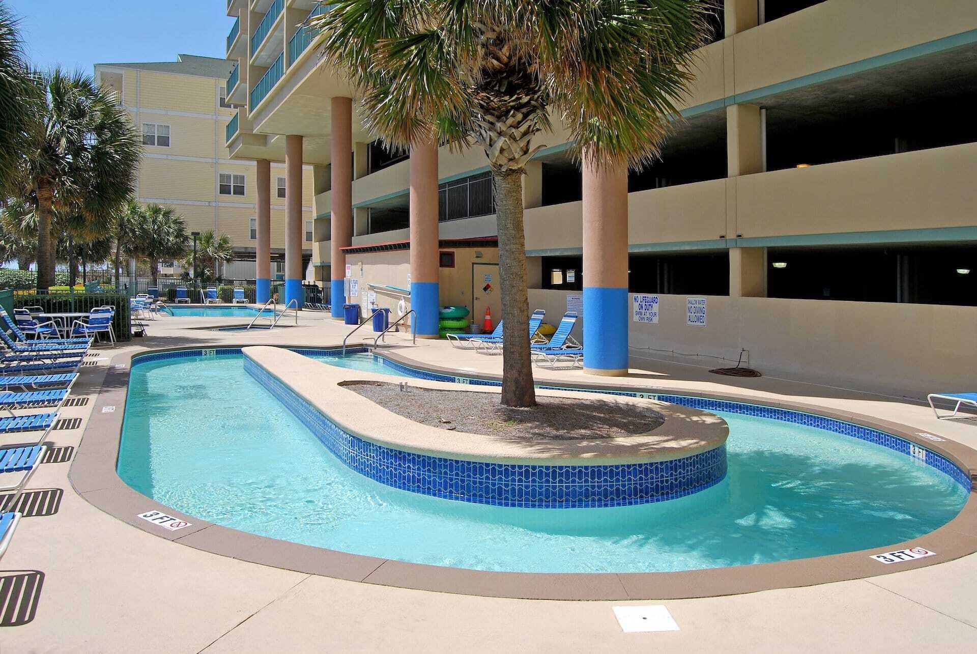 Ein Swimmingpool mit blau gefliesten Rändern, umgeben von Liegestühlen und Palmen.