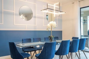 Un salón de conferencias con una mesa de vidrio, sillas azules, un jarrón con flores blancas y una lámpara moderna.