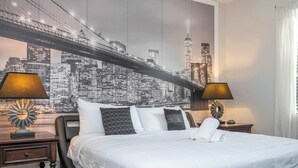 Une chambre d’hôtel avec un grand lit, deux tables de chevet et une fresque représentant un paysage urbain sur le mur.