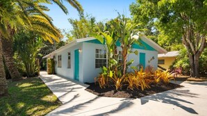 A single-story house with a white exterior and teal accents, surrounded by lush greenery and palm trees. - King Bed Near Pickleball, Beach & Downtown (Naples)