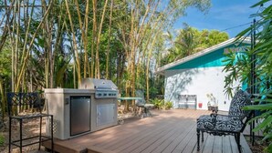A wooden deck with a barbecue grill, a chair, and a building in the background. - King Bed Near Pickleball, Beach & Downtown (Naples)