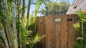 A wooden gate with a sign that says "Enjoy" in a garden setting with bamboo and palm plants. - King Bed Near Pickleball, Beach & Downtown (Naples)