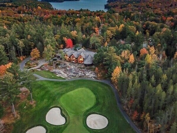 A golf course with a house surrounded by dense forest.