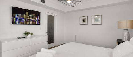 Una habitación de hotel moderna con una cama grande, un televisor de pantalla plana montado en la pared, una lámpara de techo original y una puerta que da a otra habitación.