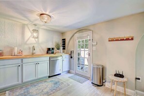 Una cocina moderna con armarios blancos, encimera de madera, candelabro y puerta que da a un área exterior.