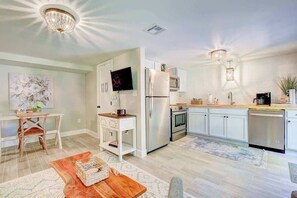 A modern kitchen with white cabinets, stainless steel appliances, a dining area with a wooden table, and a chandelier.
