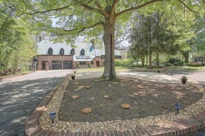 A large building with a brick facade, a central tree, and a paved driveway.