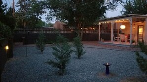 Een overdekt terras met tafel en stoelen, omringd door bomen en een grindpad.