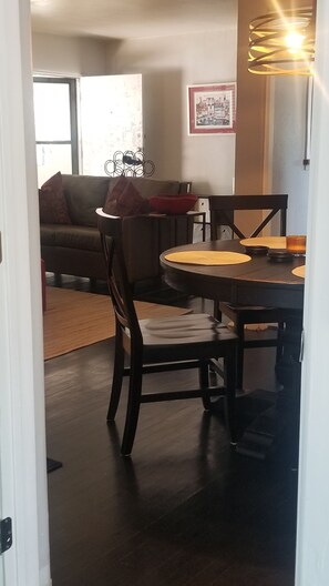 Un coin repas avec une table et des chaises en bois foncé, ainsi qu’une bougie. On aperçoit un canapé et un tableau encadré à l’arrière-plan.