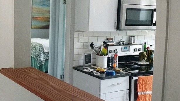 Een keuken met witte kastjes, een magnetron en een houten plank.