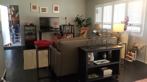 Een woonkamer met een bank, een televisie, een rode schaal, een plant en een lamp.