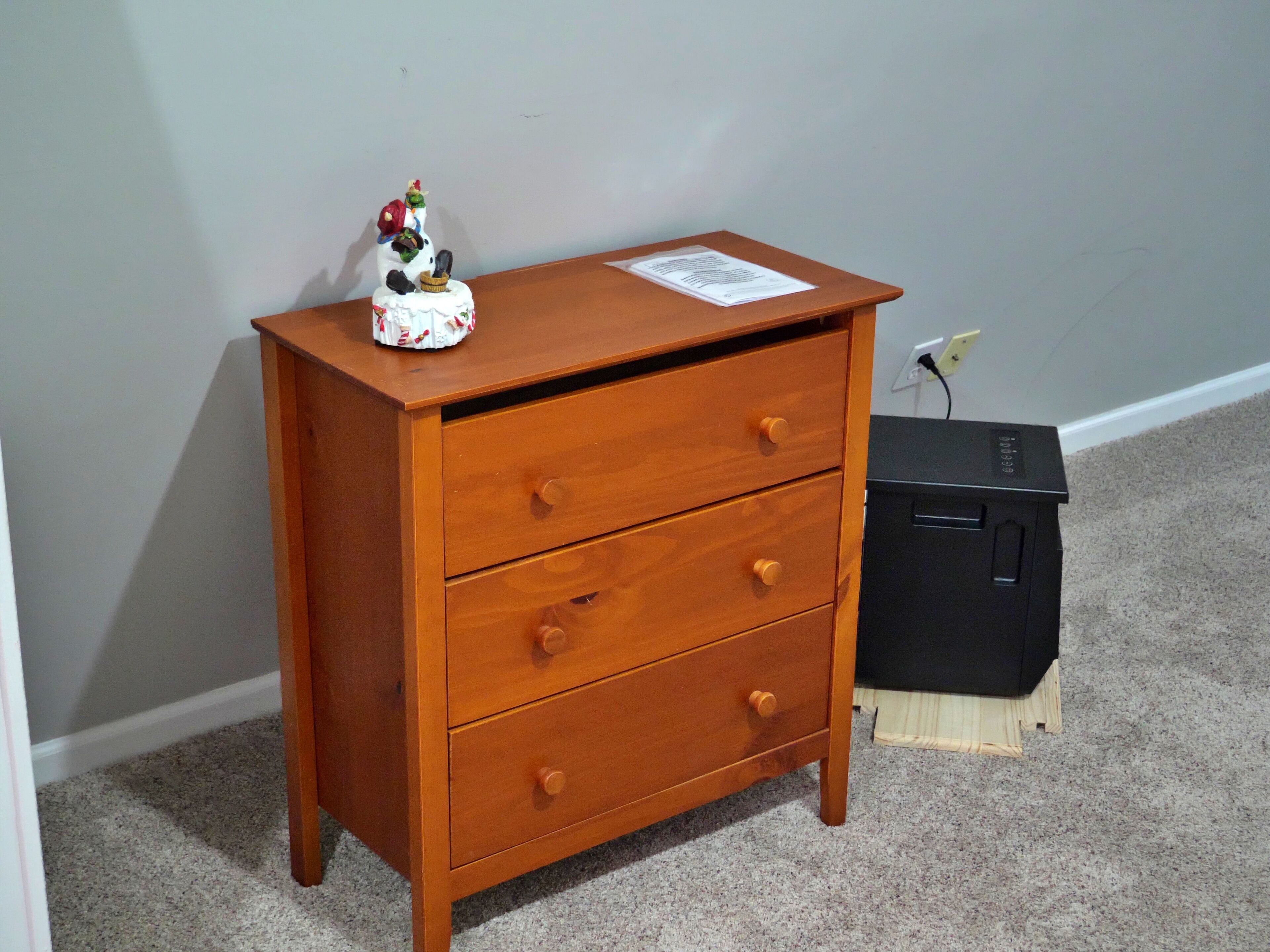 Een houten dressoir met drie lades en een klein beeldje erboven.
