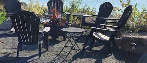 An outdoor seating area with Adirondack chairs and a small table, overlooking a lake.